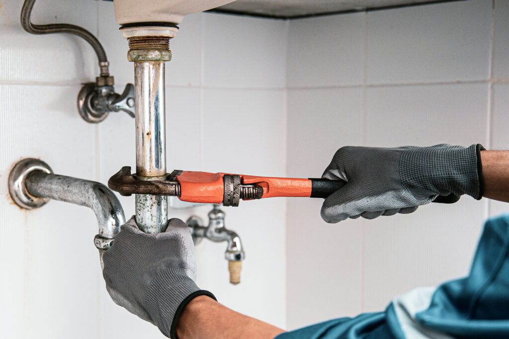 technician plumber using a wrench to repair a water pipe under t